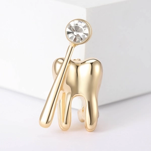 Dettaglio di una spilla a forma di dente dorato e specchio dentale con zircone lucido