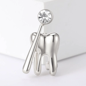 Dettaglio della spilla a forma di dente e specchio in metallo lucido con zircone puro