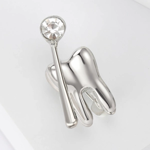 Dettaglio di una spilla a forma di dente in argento con specchio dentale e zircone lucido
