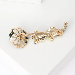 Élégante broche feuille et grenouille dorée avec détails en émail sur socle blanc