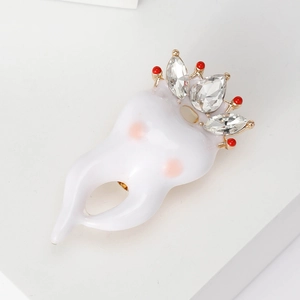 Broche créative en forme de dent avec couronne dorée et strass sur fond blanc pur