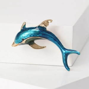 Minimalist gold and gradient blue enamel dolphin brooch pin on a white platform