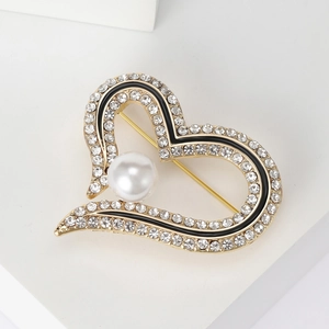 Détail d'une broche cœur dorée avec perle blanche, émail noir et cristaux brillants
