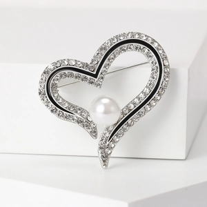 Détail d'une broche en cœur avec strass blancs, émail noir et perle centrale