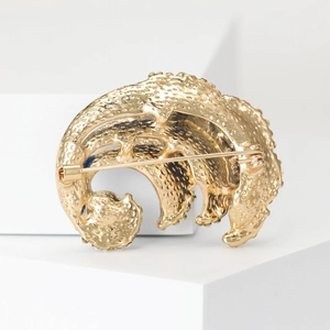 Artistic golden ocean wave brooch with blue enamel details and pearl accents on white pedestal