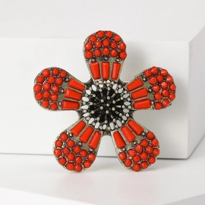 Detail einer Vintage-Blumenbrosche mit roten Perlen und schwarzer Mitte auf weiß