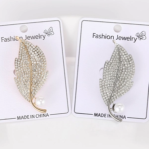 Close-up of leaf brooches with rhinestones and pearls in gold and silver finishes
