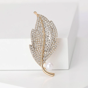 Detailed view of leaf-shaped gold brooch with inlaid rhinestones and a white pearl