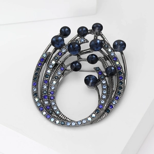 Elegant swirl-shaped brooch with deep blue crystals on a modern geometric display