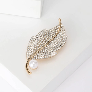 Close-up of golden leaf brooch with sparkling crystals and a round white pearl