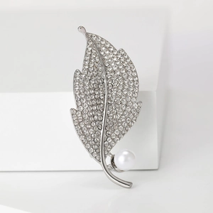 Close-up of silver leaf brooch with sparkling rhinestones and a white pearl on a white step