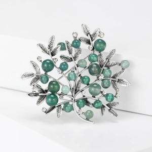 Detailed macro view of silver tree brooch with green pearls and sparkling rhinestones