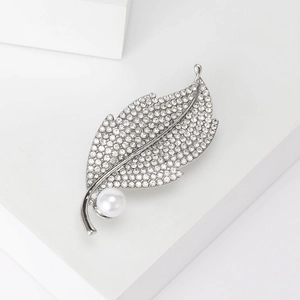 Elegant silver leaf brooch with sparkling rhinestones and white pearl on white pedestal