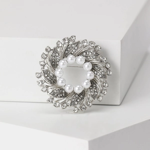 Detailed macro view of a silver floral wreath brooch with white pearls and sparkling rhinestones