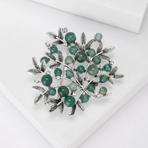 Close-up of vintage branch brooch with green beads and rhinestones on a white podium