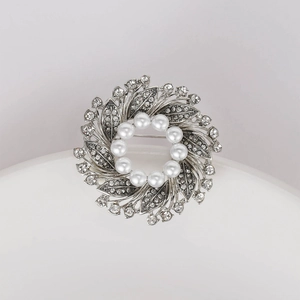 Detailed close-up of a silver floral wreath brooch with white pearls and sparkling rhinestones