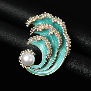 Macro detail of wave brooch with teal enamel, sparkling zircons, and a large white pearl