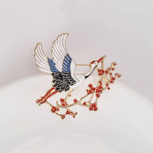 Detailed view of enamel crane and plum blossom brooch with gold branch and floral accents
