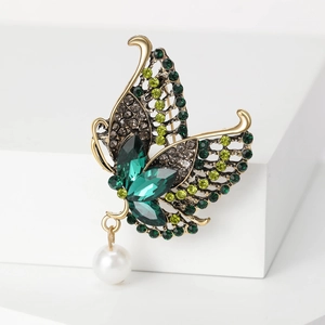 Detailed macro of golden alloy butterfly brooch with green crystals and pearl drop
