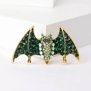 Gothic bat brooch with green crystals and golden alloy finish on a white stone base