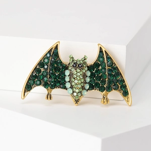 Macro detail of bat brooch featuring green rhinestones and golden metal base