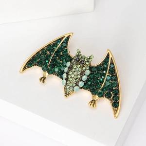 Close-up of golden bat brooch featuring intricate green rhinestones on white display