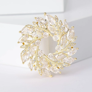 Vue macro d'une broche couronne de blé dorée avec zircons marquise sur blocs blancs