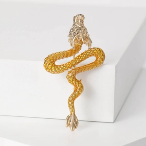 Macro shot of gold-plated dragon brooch with yellow enamel scales on white blocks