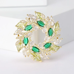 Broche couronne en zircon doré avec pierres émeraudes et jaunes sur socle blanc