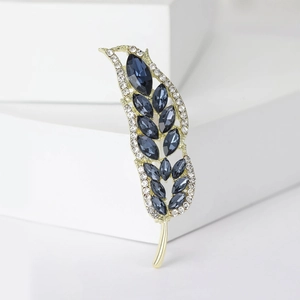 Dettaglio ravvicinato di una spilla a forma di piuma con strass blu e placcatura oro
