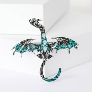 Detailed dragon brooch with peacock green enamel wings and blue crystals on a white stone