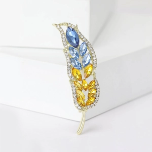 Elegante spilla a forma di grano dorata con strass blu e gialli su espositore bianco