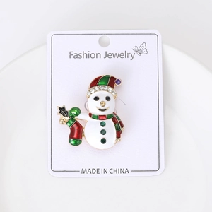 Détail d'une broche bonhomme de Noël avec chapeau en émail rouge sur carte blanche