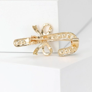 Back view of gold candy cane brooch with bow on a minimalist white block display
