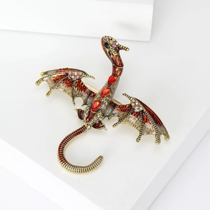 Detail of dragon brooch with red teardrop gemstones and enamel wings on white stone