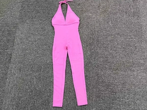 Flat lay of a pink sleeveless yoga jumpsuit with tie-back detail on a grey background
