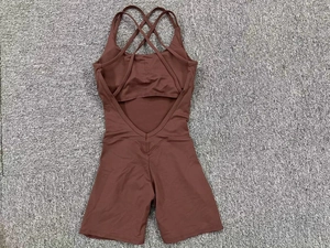 Flat lay of brown one-piece yoga romper with cross back straps on a gray textured background