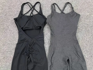 Flat lay of black and grey scrunch butt yoga jumpsuits with cross back detail on grey carpet