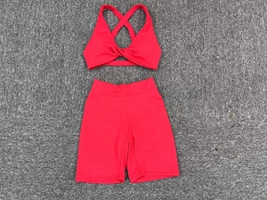 Flat lay of coral red two-piece yoga set with cross back bra and high-waist cycling shorts
