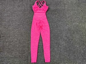 Pink ribbed yoga jumpsuit featuring cross-back straps and scrunch butt detail on grey mat