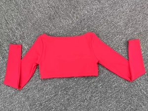Top corto de yoga rojo de manga larga con cuello cuadrado sobre fondo gris texturizado
