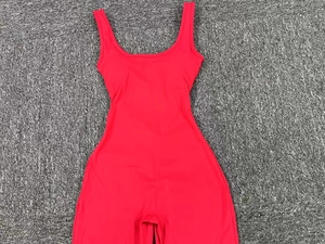 Close-up of a red backless yoga bodysuit laid on a textured grey carpet background