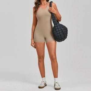 Front view of a woman in a tan halter neck yoga romper with a matching stylish bag