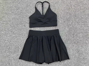 Flat lay of black sports bra and pleated tennis skirt set on a grey textured surface