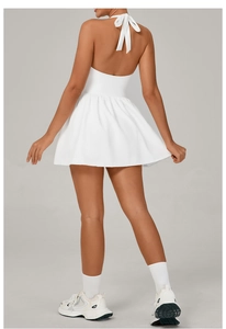 Back view of a white halter tennis dress with cross-tie bow design and pleated skirt