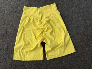 Gros plan détaillé du short de yoga taille haute jaune vif avec effet froncé sur tapis gris