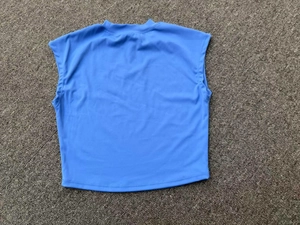 Flat lay of a sky blue slim fit athletic crop top with sleeveless design on a knit rug