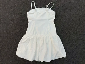 Flat lay of a white sleeveless golf dress with adjustable straps and bubble hem detail