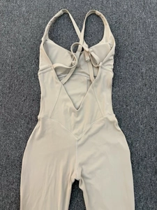 Detailed back view of beige yoga bodysuit featuring adjustable crisscross straps and metal buckles