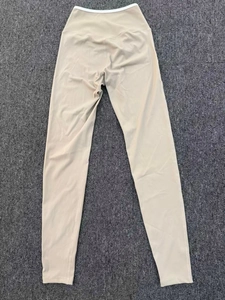 Flat lay detail of beige high waisted yoga pants with white waist piping on textured background